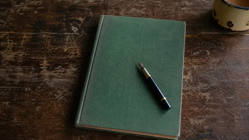 A closed cloth-bound register and a pen resting on a worn wooden desk in a school staffroom.