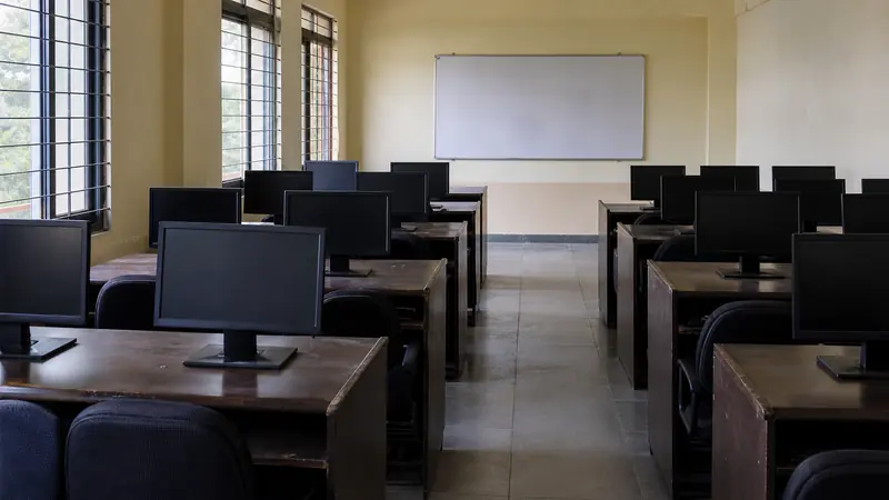Rows of empty desks and switched-off monitors in a school computer lab arranged for a staff training session.