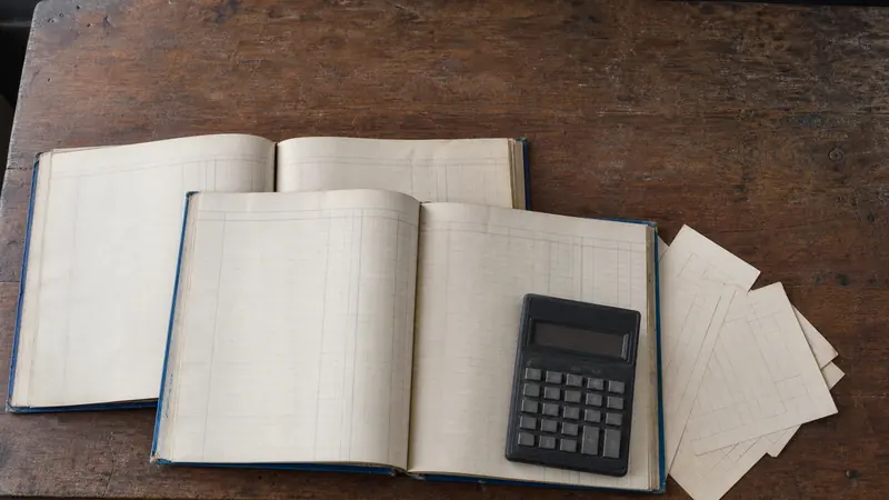 Open ledger volumes and loose bank slips spread across a wooden desk in a school office, a calculator resting on top.