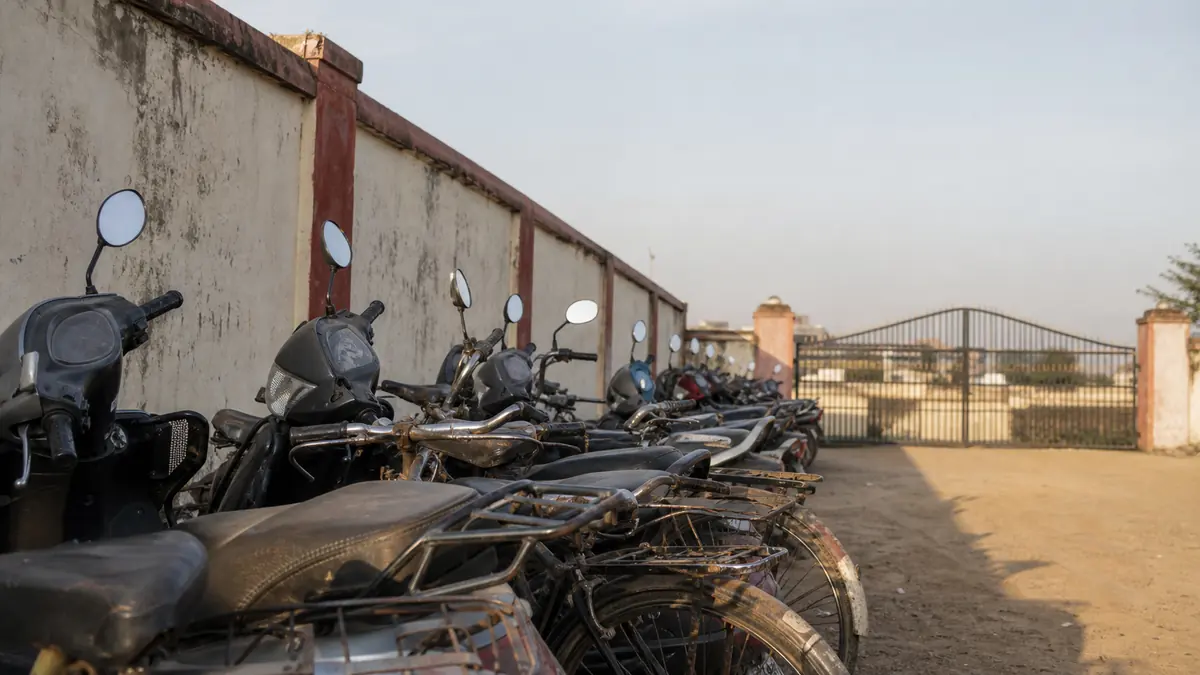 Early morning outside an Indian school gate, scooters parked along the boundary wall before the bell.