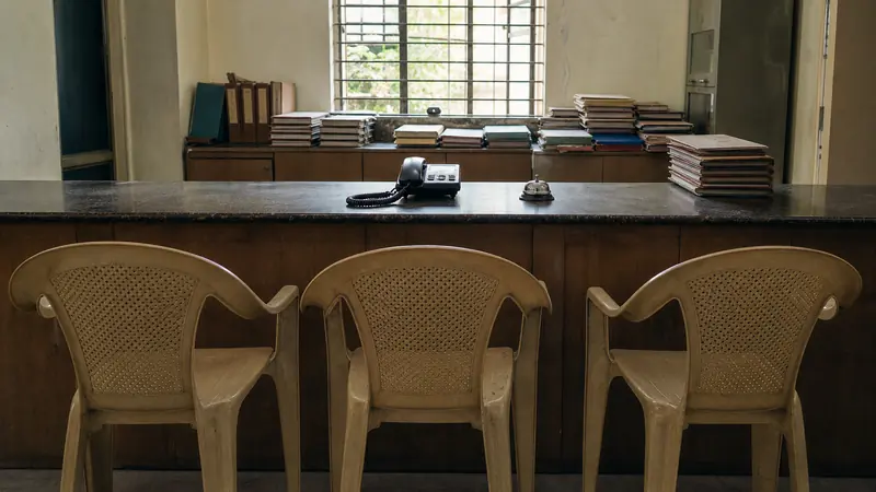 A front-office counter in an Indian school with a landline telephone, stacked files, and empty visitor chairs.